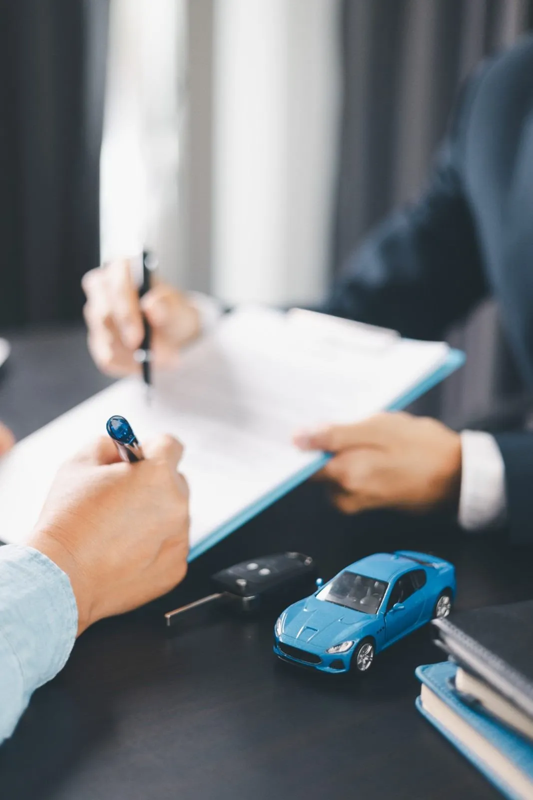Person signing a vehicle contract beside a set of car keys